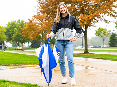Student wearing black and gray rain jacket holding GV Umbrella